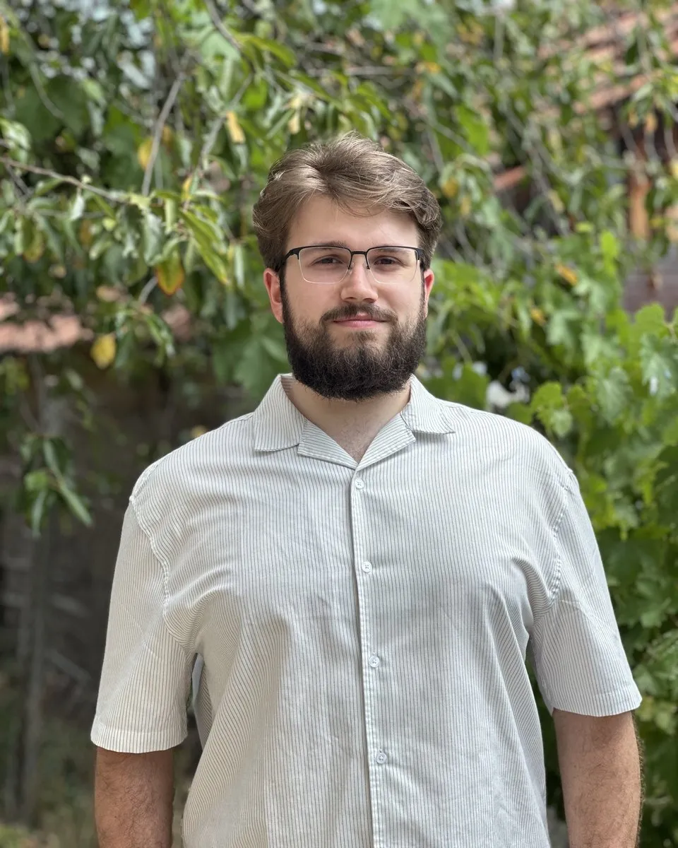 Vuk Aranđelović outdoors in front of green leaves, smiling at the camera
